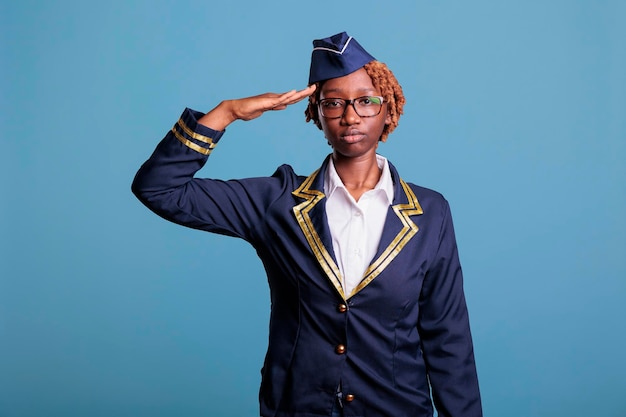 Portret van vrouwelijke stewardess zwaaiend gekleed in luchtvaartuniform. African american vrouw stewardess kijken vol vertrouwen naar camera in studio opname met blauwe achtergrond.