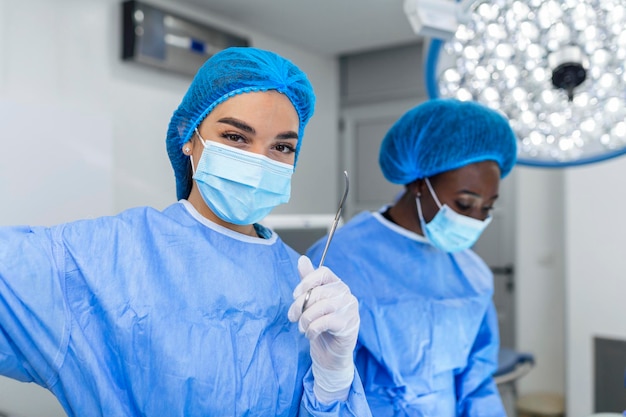 Portret van vrouwelijke vrouw verpleegster chirurg of personeelslid gekleed in chirurgische scrubs toga masker en haarnet in ziekenhuis operatiekamer theater maken oogcontact glimlachend blij gelukkig camera kijken