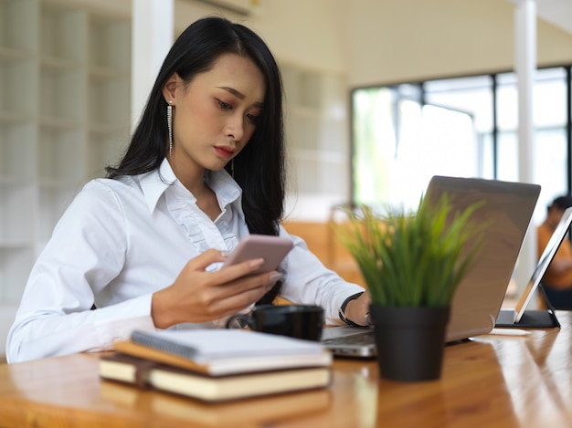 Portret van vrouwelijke werken met smartphone, laptop en boeken in co werkruimte