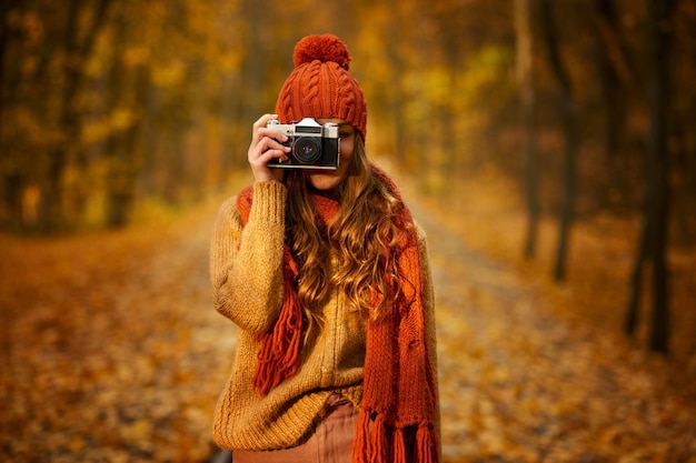 Foto portret van vrouwenfotograaf die retro camera houdt. meisje in de herfstpark. onscherpe achtergrond