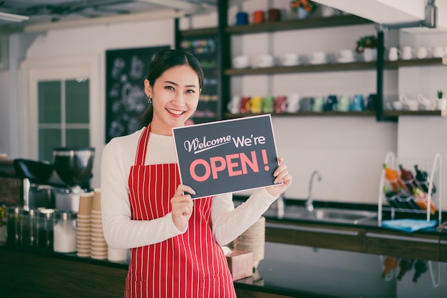 Portret van vrouwenserveerster die zich bij haar koffiewinkelpoort bevindt met het tonen van open uithangbord