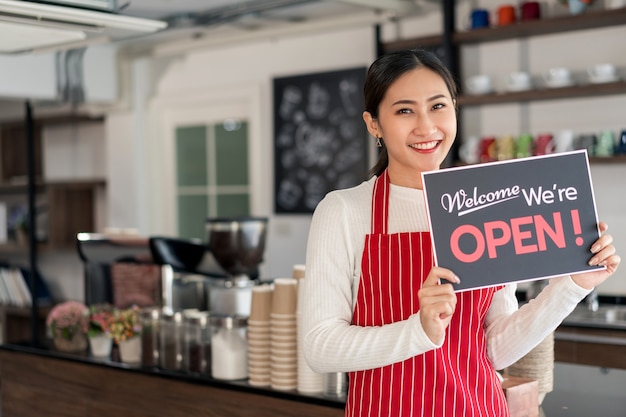 Portret van vrouwenserveerster die zich bij haar koffiewinkelpoort bevindt met het tonen van open uithangbord