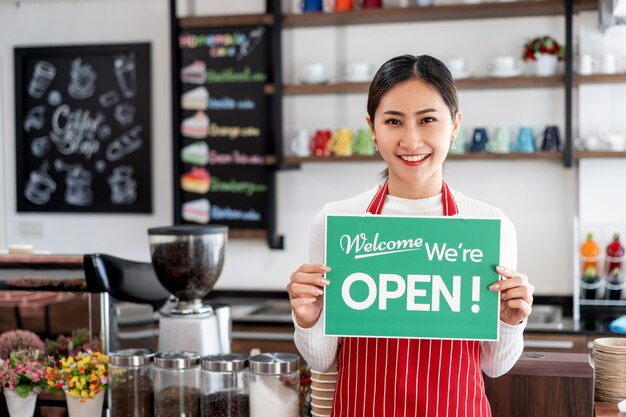 Portret van vrouwenserveerster die zich bij haar koffiewinkelpoort bevindt met het tonen van open uithangbord