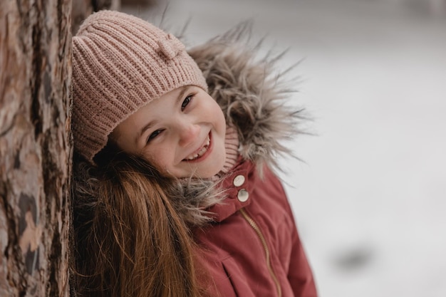 Portret van weinig aanbiddelijk meisje in de winterhoed bij sneeuwbos