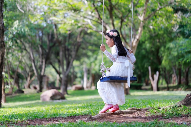 Portret van weinig Aziatisch meisje dat de schommeling speelt onder de grote boom in het aardbos
