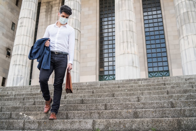 Portret van zakenman die gezichtsmasker draagt en van de trap loopt die aktentas houdt op weg naar het werk