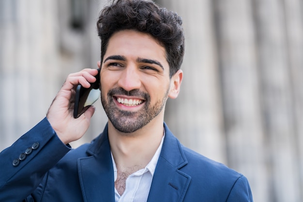 Portret van zakenman praten aan de telefoon terwijl hij buiten op straat staat. Bedrijfs- en succesconcept.