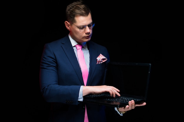 Portret van zekere knappe ernstige zakenman die laptop tonen die op zwarte achtergrond wordt geïsoleerd