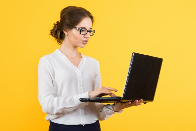 Portret van zekere mooie jonge bedrijfsvrouw die aan laptop op gele t-shirt werkt