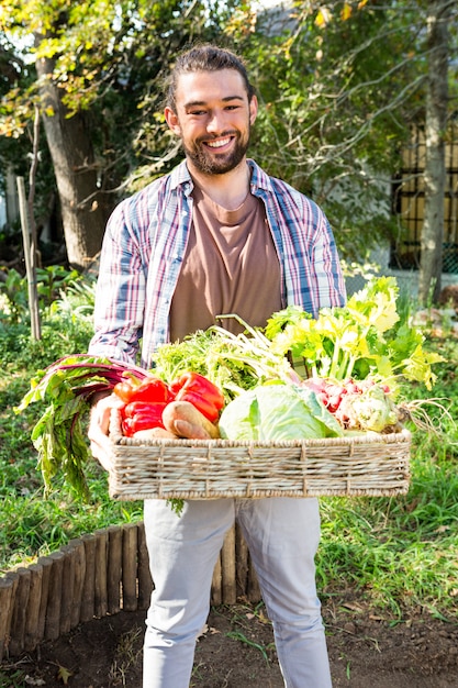 Portret van zekere tuinman met groenten in mand bij tuin