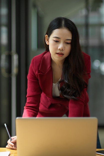 Portret van zelfverzekerde en slimme jonge Aziatische zakenvrouwen die op haar laptop op kantoor werken