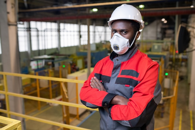 Portret van zelfverzekerde jonge Afrikaanse man in gasmasker en veiligheidshelm werken bij giftige industrie