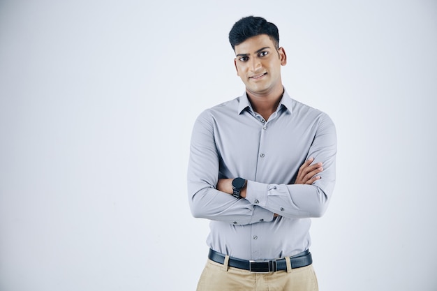 Portret van zelfverzekerde jonge Indiase ondernemer die de armen oversteekt en naar de camera glimlacht