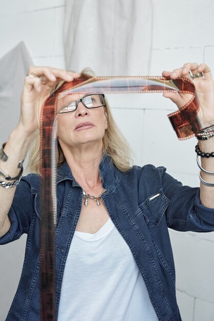 Portret van zelfverzekerde volwassen fotograaf in spijkerjasje die aan tafel staat en foto's kiest voor album