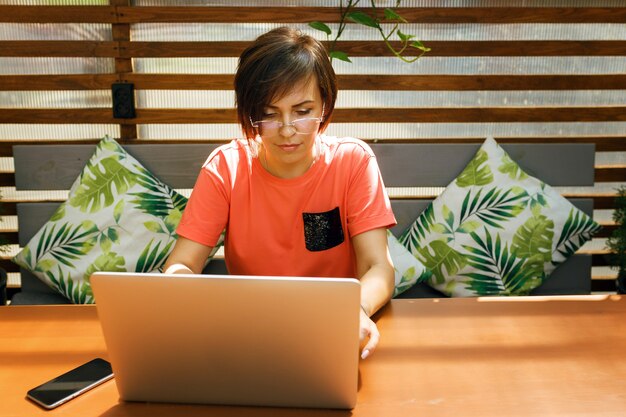 portret van zelfverzekerde volwassen professionele vrouw zittend op het zomerterras in café met behulp van laptop
