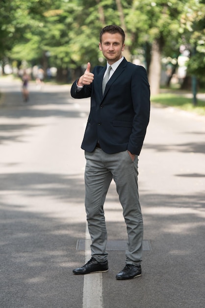 Portret van zelfverzekerde zakenman terwijl hij buiten in het park staat met duimen omhoog teken