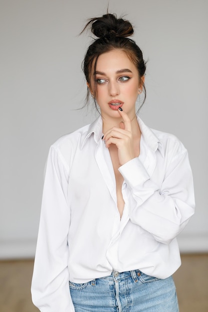 Portret van zittende jonge vrouw, gekleed in een bouffant shirt met blote schouders op lichtgrijze achtergrond mooi brunette meisje in jeans en witte tshirt glimlachen