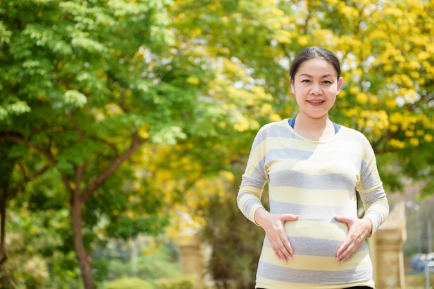 Portret van zwangere Aziatische vrouw lachend, met een natuurlijke achtergrond.