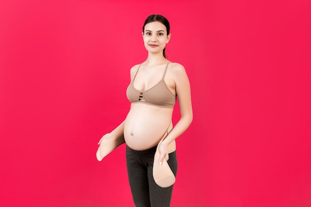 Portret van zwangere vrouw bij het opzetten van ondersteunend verband voor het verminderen van rugpijn op roze oppervlak met kopie ruimte