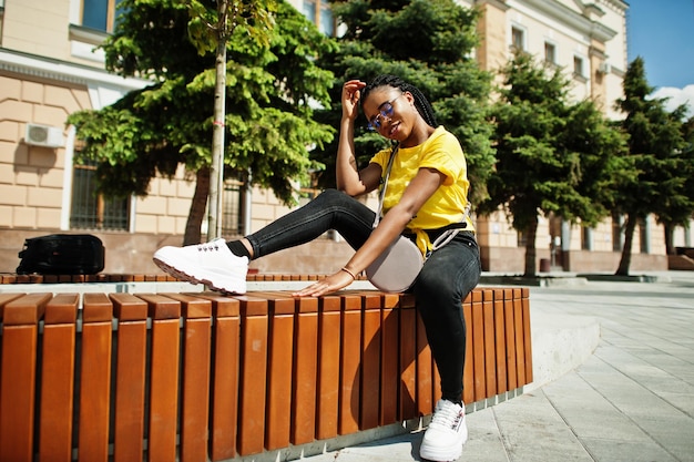 Portret van zwarte Afro-Amerikaanse vrouw in geel t-shirt en bril.