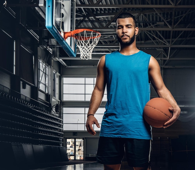 Portret van zwarte basketbalspeler houdt een bal over een hoepel in een basketbalhal.