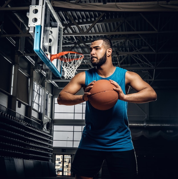 Portret van zwarte basketbalspeler houdt een bal over een hoepel in een basketbalhal.