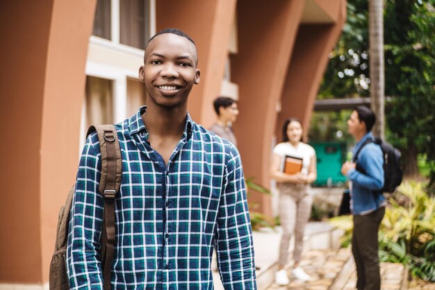 Portret van zwarte jonge man student met universiteit op achtergrond