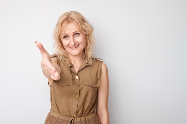 Portret volwassen vrouw kiest je geïsoleerd op witte studio achtergrond strekt haar handpalm uit naar de camera kom met me mee bij ons concept