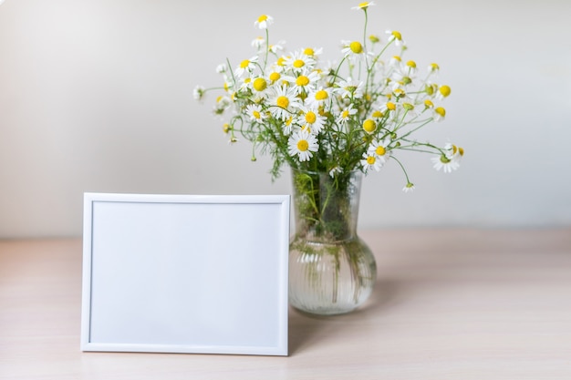 Portret witte fotolijst mockup op houten tafel glazen vaas met kamille