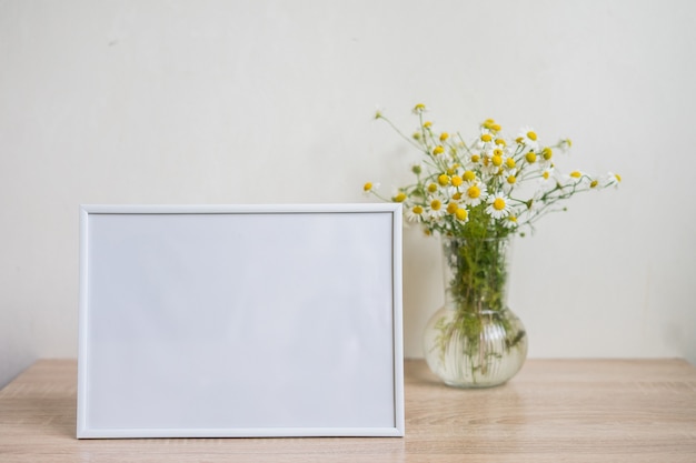 Portret witte fotolijst mockup op houten tafel glazen vaas met kamille