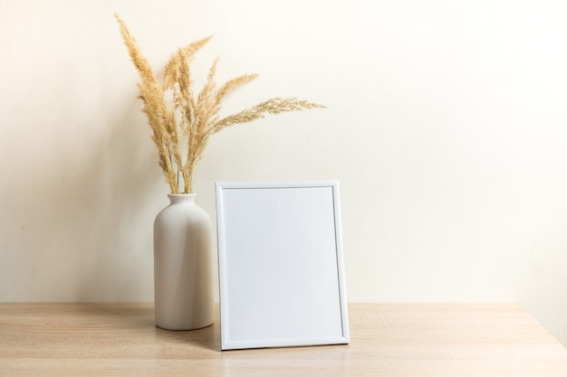 Portret witte fotolijst mockup op houten tafel Moderne keramische vaas met gedroogde bloemen