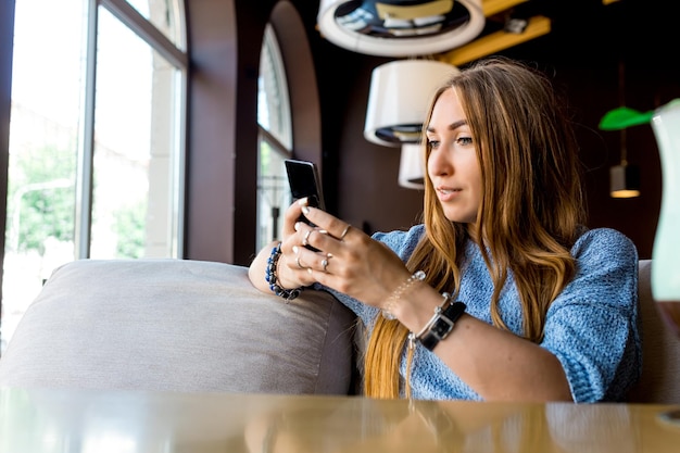 카페 톤의 선택적 포커스에서 전화로 SMS를 읽는 젊은 여성의 Portret