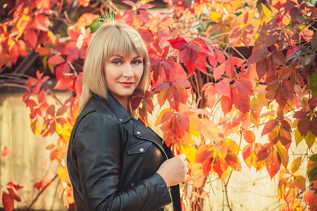 Portret of Young woman with bob haircut in a black leather jacket is standing in an abandoned greenhouse in autumn.