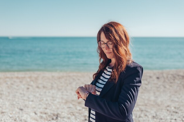 portret zakenvrouw glimlachend smartwatch controleren aan de kust