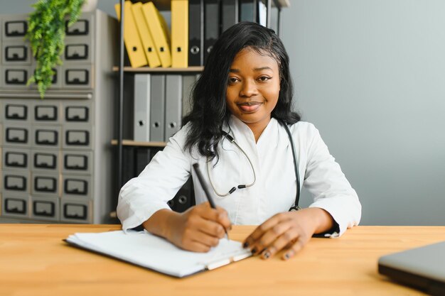 Portret zelfverzekerde Afrikaanse vrouwelijke arts medische professional die patiëntnotities schrijft geïsoleerd op de achtergrond van de gangramen van het ziekenhuiskliniek Positieve gezichtsuitdrukking