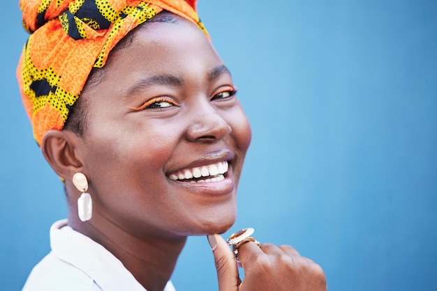 Portret zwarte vrouw en glimlach met hoofdomslag natuurlijke schoonheid of vertrouwen voor cosmetica op blauwe studio achtergrond Jamaicaans vrouwelijk meisje of jonge dame met traditionele hoofddoek stijlvol of make-up