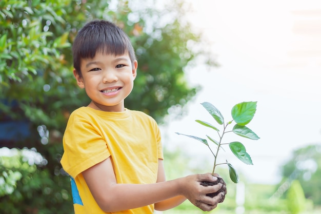 Foto portretbeeld van aziatische kindjongen die een kleine groene plant met aarde vasthoudt. groeiende boom. lente seizoen. milieu sparen. dag van de aarde. wereld dag. 7-8 jaar oud.