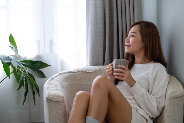 Portretbeeld van een mooie aziatische vrouw die hete koffie drinkt en thuis ontspant op een bank in de slaapkamer