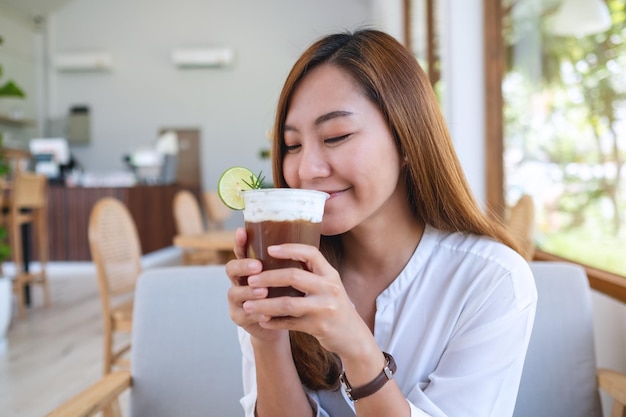 Portretbeeld van een mooie jonge aziatische vrouw die ijskoffie vasthoudt en drinkt in café