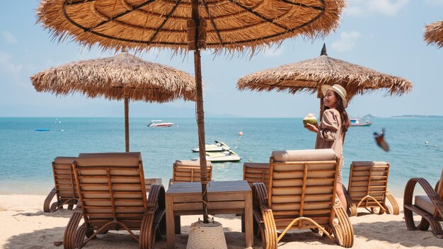 Portretbeeld van een mooie jonge aziatische vrouw die kokossap vasthoudt en drinkt op het strand