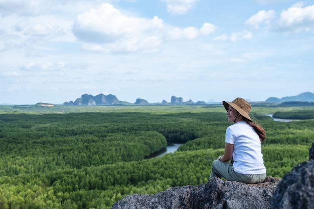 Portretbeeld van een mooie jonge aziatische vrouw die op de bergtop zit terwijl ze door het mangrovebos reist