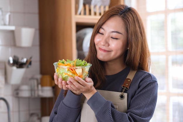 Foto portretbeeld van een mooie jonge aziatische vrouw die thuis een verse gemengde groentensalade in de keuken houdt