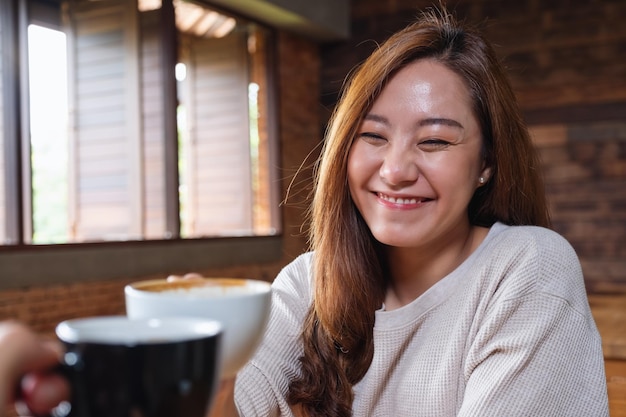 Portretbeeld van een mooie jonge aziatische vrouw en een man die samen koffiemokken rammelt in café