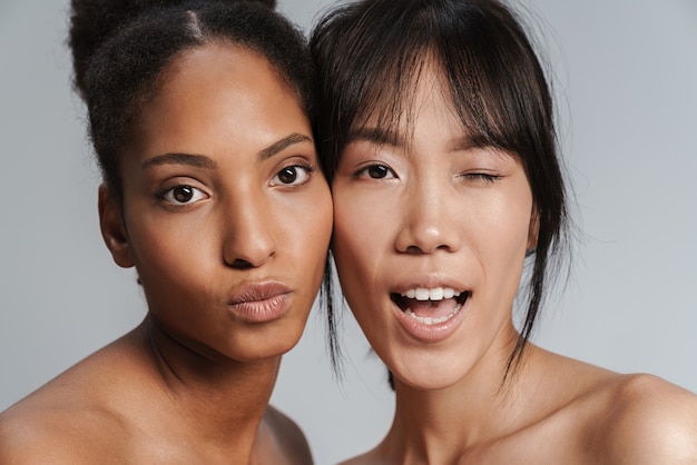 Portretclose-up van twee multinationale halfnaakte vrouwen die kuslippen maken en knipogen