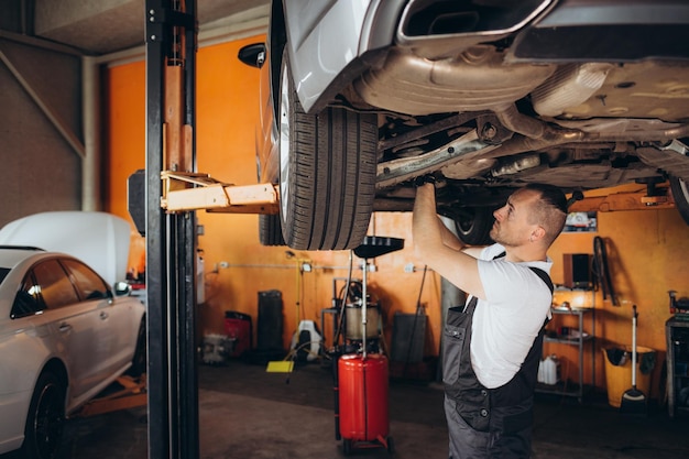 Portretfoto van een knappe monteur die aan een voertuig werkt in een auto-service Professionele monteur draagt handschoenen en gebruikt een ratchet onder de auto Moderne schone werkplaats