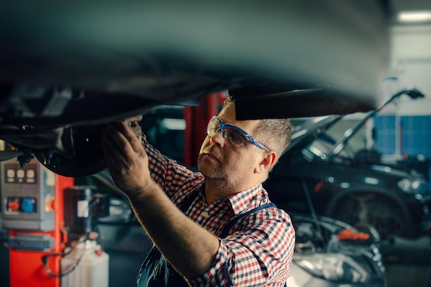 Portretfoto van een knappe monteur die aan een voertuig werkt in een autoservice