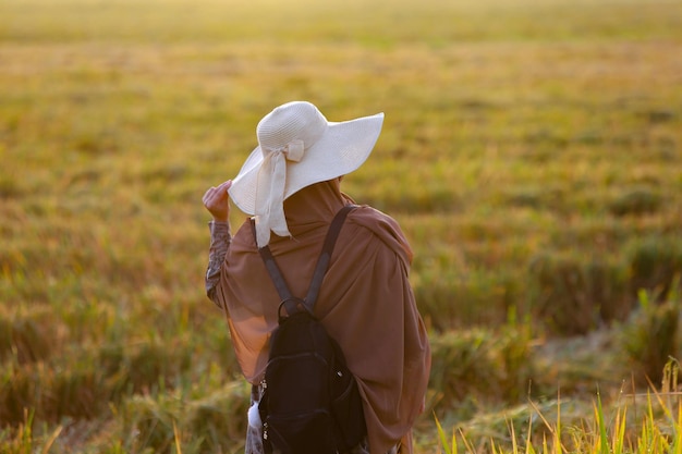 Portretfoto van een vrouw die bij zonsopgang tussen landelijke rijstvelden loopt