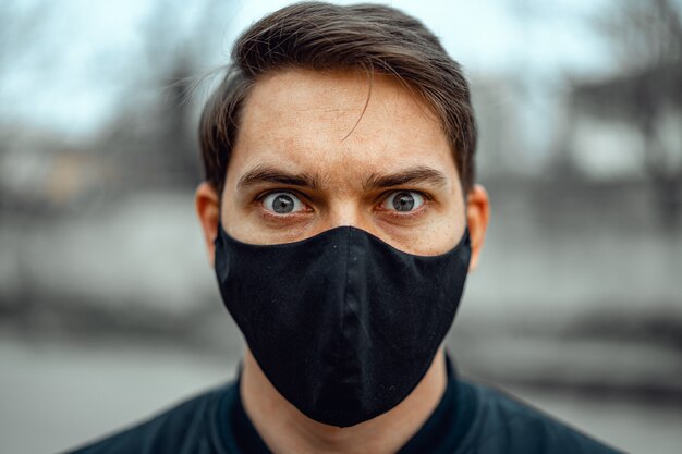 Portretmens in medisch masker. Jonge man staat op lichte achtergrond en camera kijken.