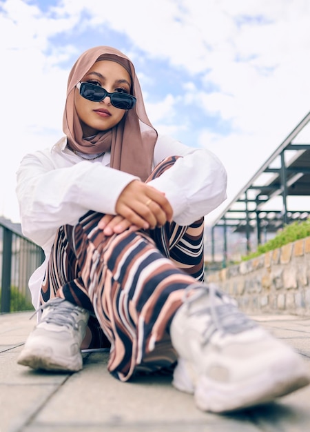 Portretmode of hijab met een islamvrouw buiten in zonnebril en sjaal voor eigentijdse stijl Arabisch geloof of boerka met een trendy jonge moslim buiten in een stad die moderne kleding draagt