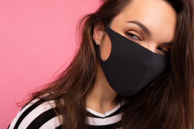 Portretschot van jonge aantrekkelijke vrouw die mediacal zwart gezichtsmasker draagt dat over achtergrond wordt geïsoleerd